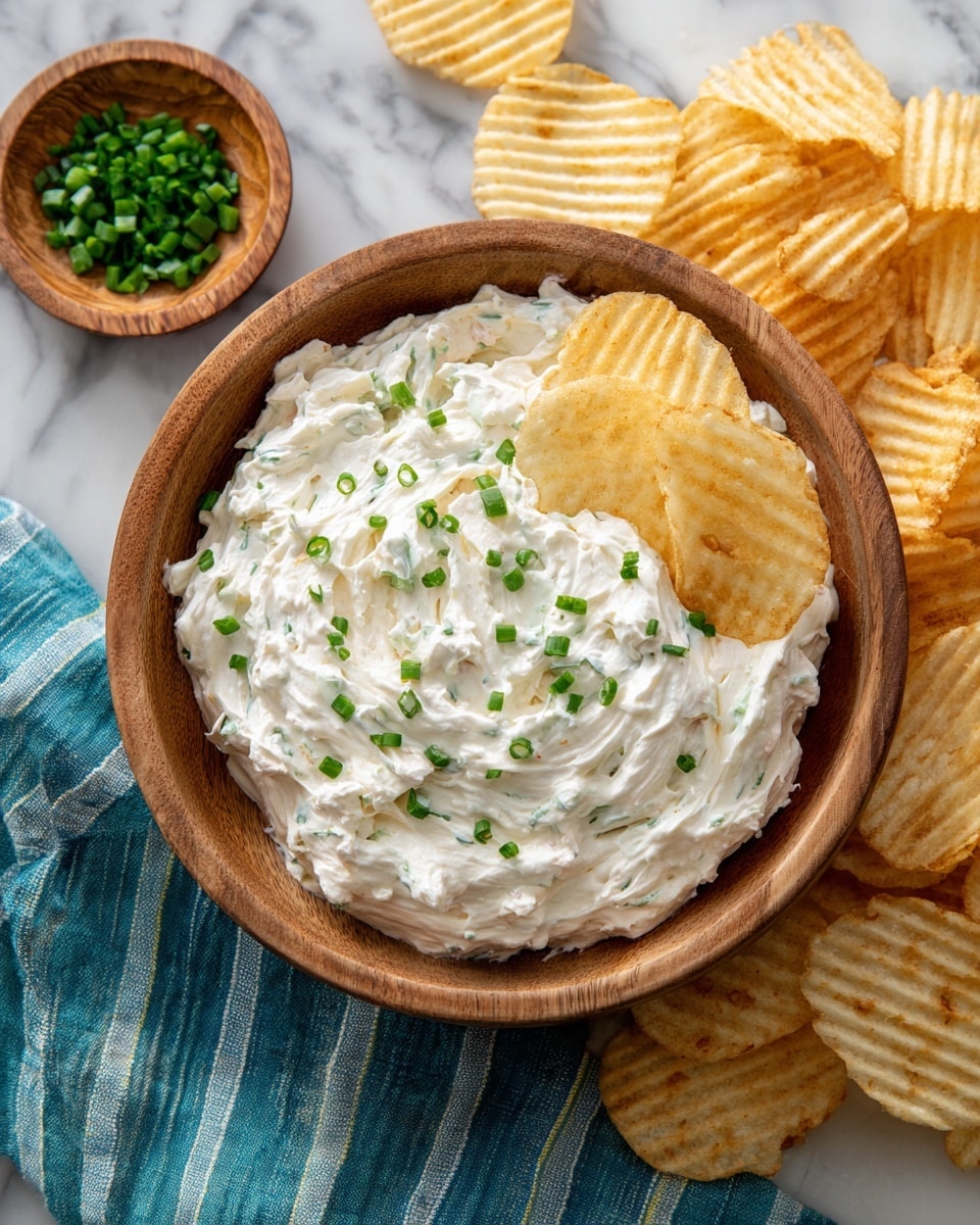A wooden bowl filled with a creamy white dip that has small pieces of mushrooms mixed inside, with green chopped chives sprinkled on top. Two thick, ridged potato chips are placed on the right edge of the bowl, partially dipped in the sauce. Around the bowl, there are many similar thick, ridged potato chips scattered on a white marbled surface. In the top left corner, there is a round wooden plate with a pile of chopped green chives. A blue cloth is partially visible in the bottom left corner on the white marbled surface. photo taken with an iphone --ar 4:5 --v 7