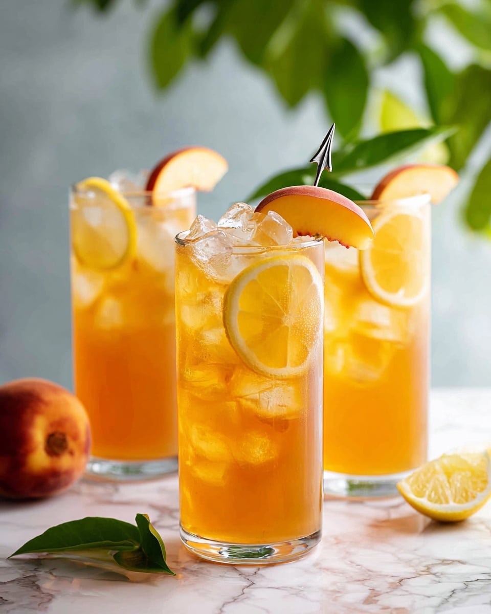 Three tall clear glasses filled with light pink peach drink and large ice cubes are placed on a white marbled surface. Each glass has one slice of yellow lemon inside, visible through the drink, and a large slice of fresh peach is placed on the rim of each glass with a small silver drink pick. The glasses are arranged with one in the front right corner and two others slightly blurred in the background. Green leafy plants are softly visible in the background. The lighting is bright and natural photo taken with an iphone --ar 4:5 --v 7