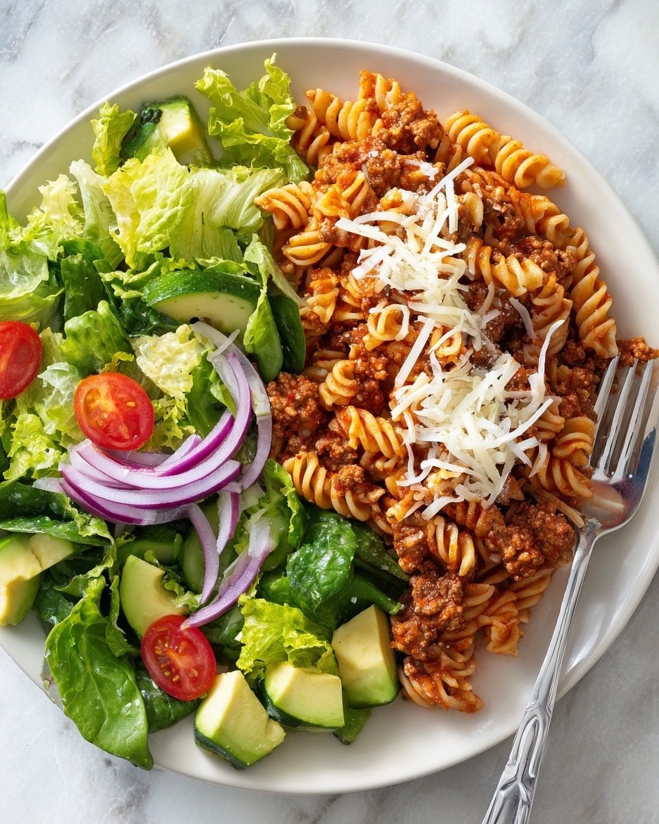 A white plate holds a colorful meal with two main parts: on the right, a layer of curly pasta mixed with a thick reddish-brown meat sauce topped with shredded white cheese; on the left, a fresh salad made of light green lettuce, pale green avocado cubes, dark green cucumber slices, red tomato pieces, and thin slices of purple onion, all arranged neatly. A silver fork rests on the plate to the right side. In the background, there is a white marbled surface with a halved avocado positioned behind the plate. photo taken with an iphone --ar 4:5 --v 7