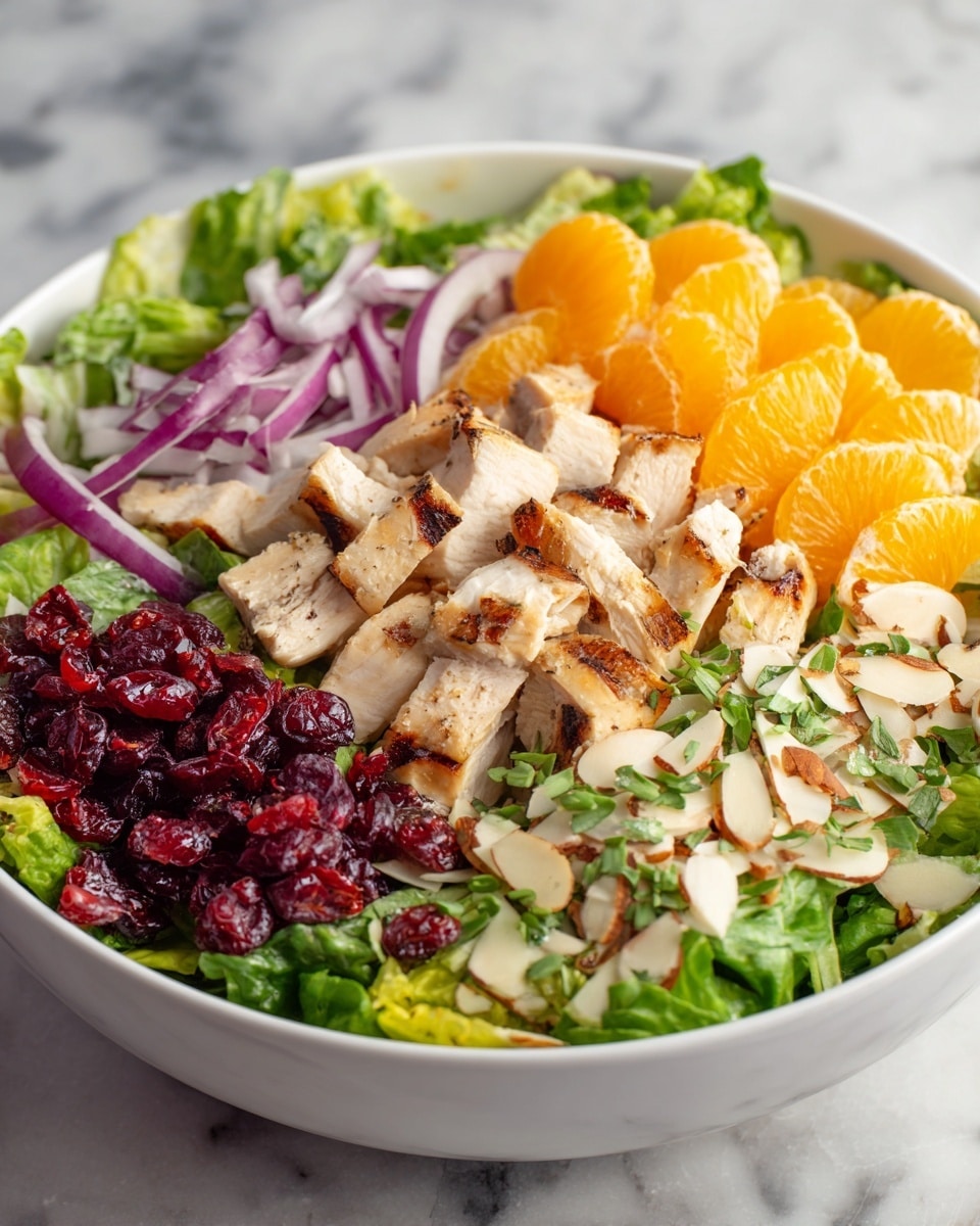 The image shows a white bowl filled with a colorful salad. The salad has several layers, starting with a bed of light green shredded lettuce at the bottom. On top of the lettuce are pieces of cooked chicken with a light brown color, spread across the salad. There are bright orange slices of mandarin, thin purple strips of onion, and small red dried cranberries scattered evenly. Pine nuts and sliced almonds add a beige, crunchy texture on the top layer. The salad looks fresh and well mixed, all placed on a white marbled surface. Photo taken with an iphone --ar 4:5 --v 7