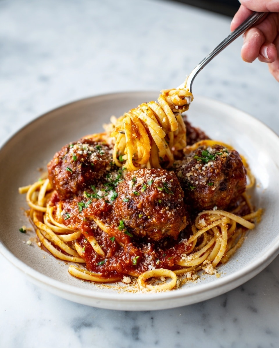 A white plate with small raised dots around the edge holds a serving of spaghetti topped with three large meatballs covered in red tomato sauce. The spaghetti is spread evenly in a circular shape, with some strands wrapped around a fork placed on the right side of the plate. The sauce has a thick texture, and there are small bits of green herbs sprinkled on top of the meatballs and sauce. The plate sits on a white marbled surface. photo taken with an iphone --ar 4:5 --v 7