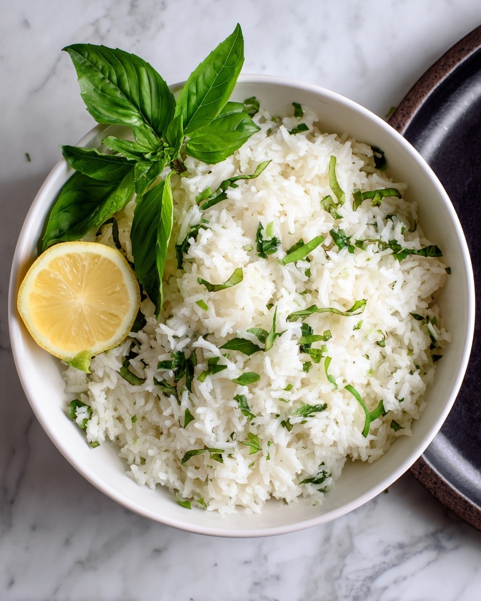 A white bowl is filled with fluffy white rice mixed with chopped green herbs, giving a light green speckled look throughout the rice. On top, there are a few fresh green basil leaves adding a pop of color. A bright yellow lemon half is placed on the side inside the bowl, contrasting with the mostly white and green dish. The bowl sits on a dark surface with a white marbled background softly visible. photo taken with an iphone --ar 4:5 --v 7