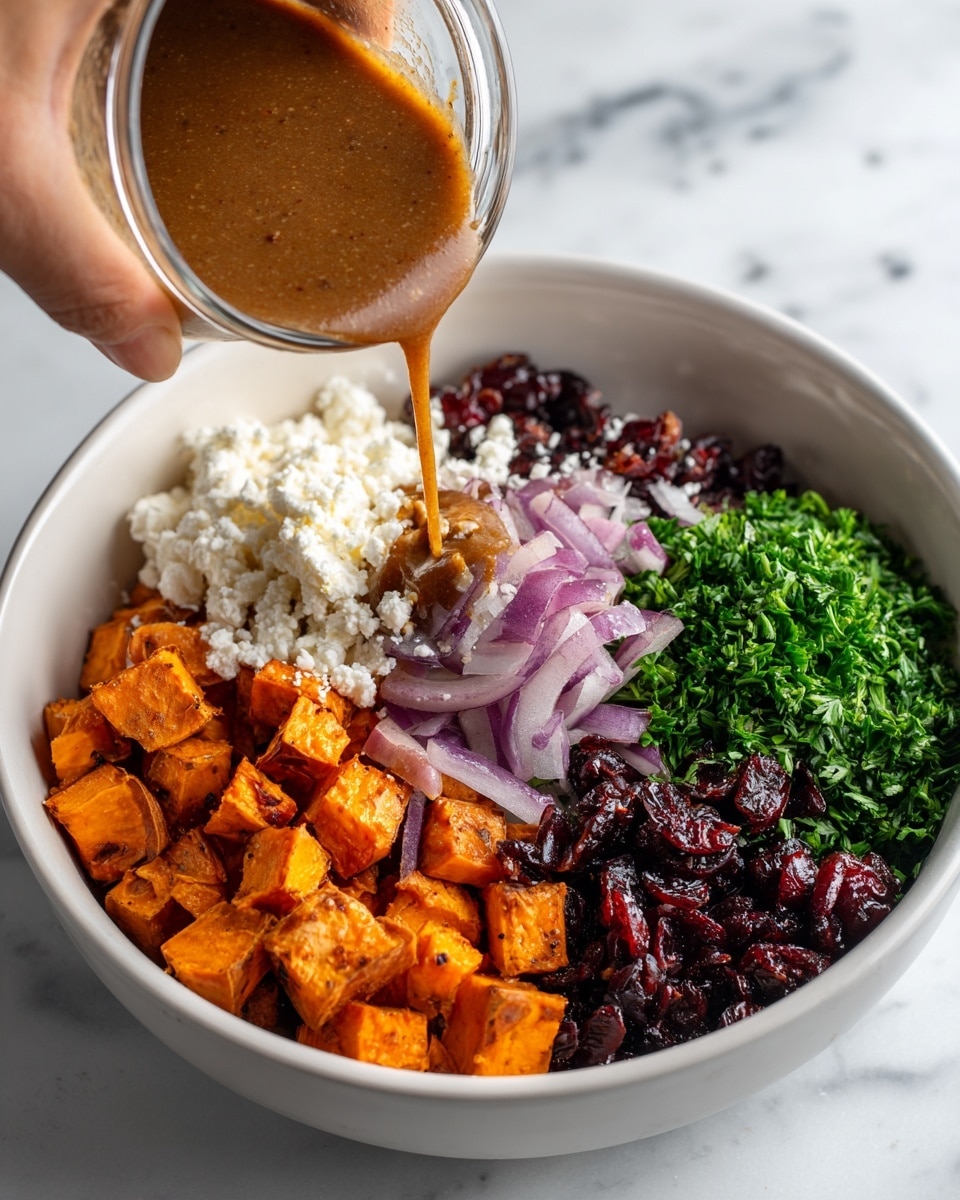 A white bowl on a white marbled surface contains five main layers arranged separately inside it. At the bottom left, there are orange roasted cubed sweet potatoes mixed with slices of caramelized purple onions. Next to it on the right, there is a layer of dark red dried cranberries. Above the cranberries, there is a pile of fresh green chopped parsley. On the top left section of the bowl, there is a large amount of crumbled white cheese. A woman's hand is pouring a smooth brown dressing from a clear glass jar onto the left side of the bowl, over the roasted sweet potatoes and cheese. Photo taken with an iphone --ar 4:5 --v 7