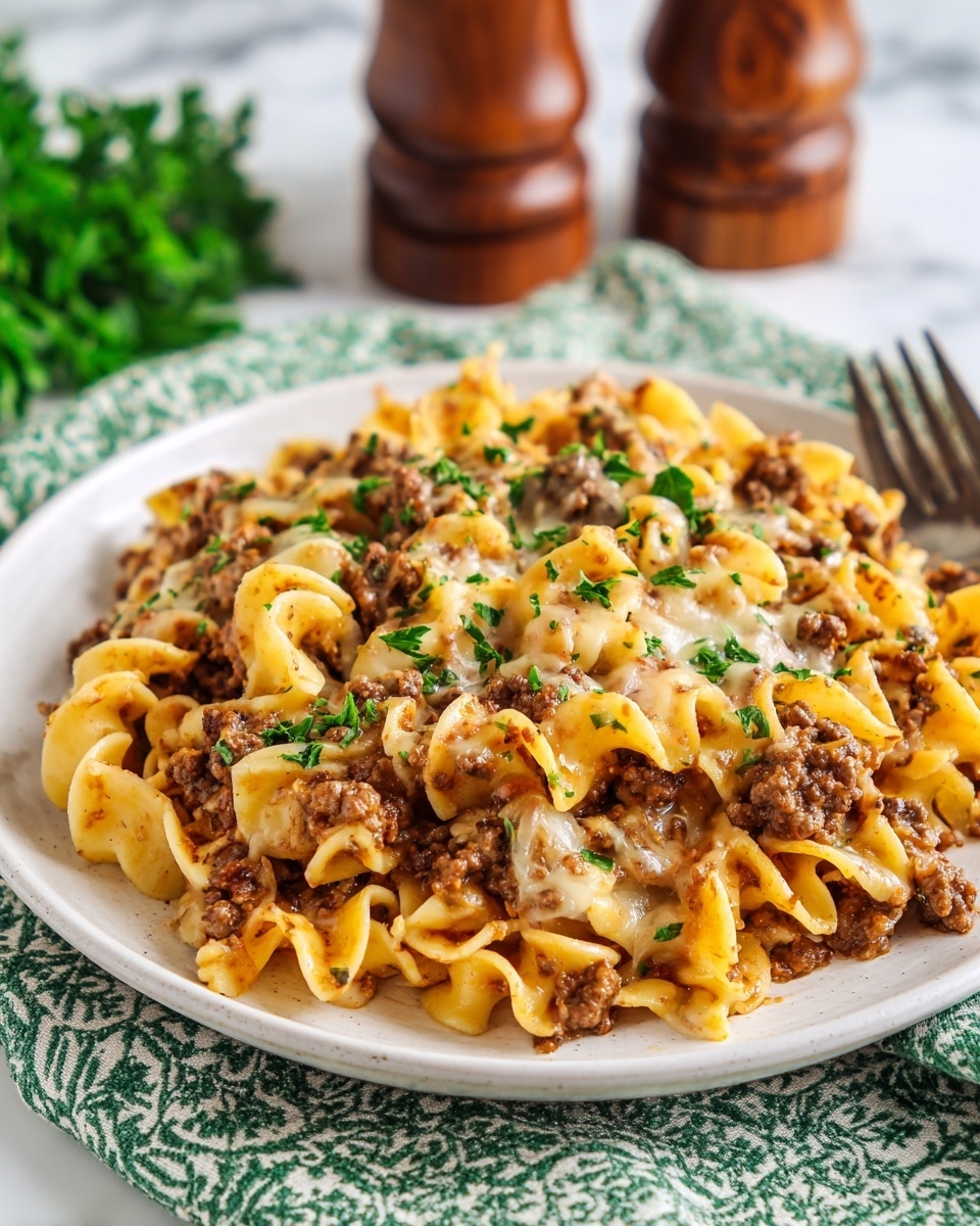 A white plate holds a three-layered pasta dish. The bottom layer is wide, curly yellow noodles mixed with small pieces of brown cooked ground meat. The second layer is more of the yellow noodles and meat, creating a thick, uneven pile. The top layer features melted light yellow cheese scattered with small bits of green herbs. The plate is placed on a green-and-white striped cloth on a wooden table, with wooden salt and pepper shakers and a white container blurred in the background. Photo taken with an iphone --ar 4:5 --v 7