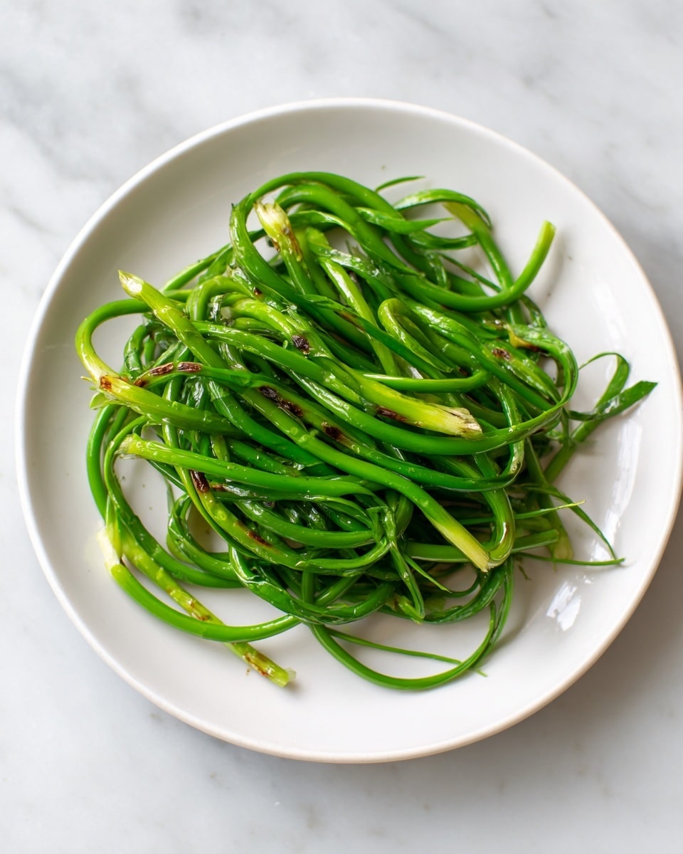 A white round plate holds a pile of bright green garlic scapes, which are long, curved, and have a smooth texture. The scapes show some light brown grilled marks, giving a slightly charred look. The plate is on a white marbled surface, and the garlic scapes are loosely arranged, showing their fresh and glossy appearance with shades of light and dark green. photo taken with an iphone --ar 4:5 --v 7