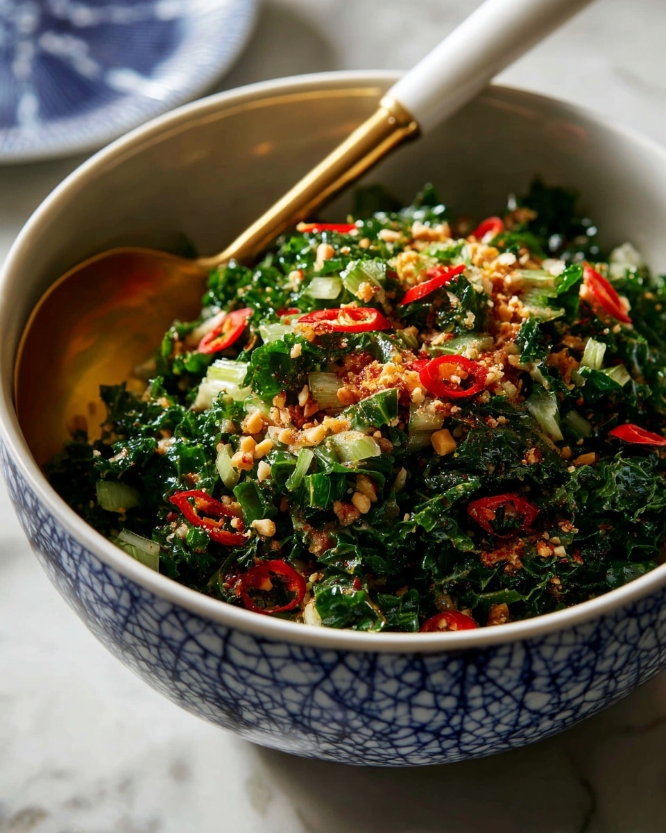 A bowl with a blue cracked pattern holds a green leafy salad mixed with small pieces of light brown nuts and slices of bright red chili peppers. The green leaves are finely chopped, with some small green stems and white bits mixed in. A spoon with a white handle and gold neck rests inside the bowl on the right side. The bowl sits on a white marbled surface. Photo taken with an iphone --ar 4:5 --v 7