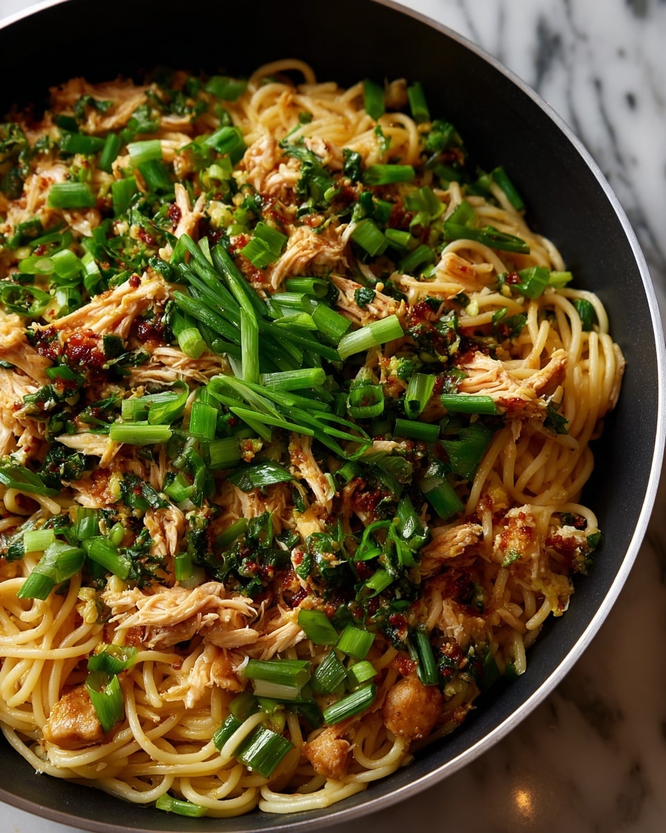 A large black pan filled with a mix of thick light brown noodles and shredded light golden chicken pieces. Scattered throughout are bright green slices of fresh scallions, adding contrast. The noodles and chicken are coated evenly in a glossy sauce, giving a slightly shiny texture. The background shows a white marbled surface beneath the pan. photo taken with an iphone --ar 4:5 --v 7