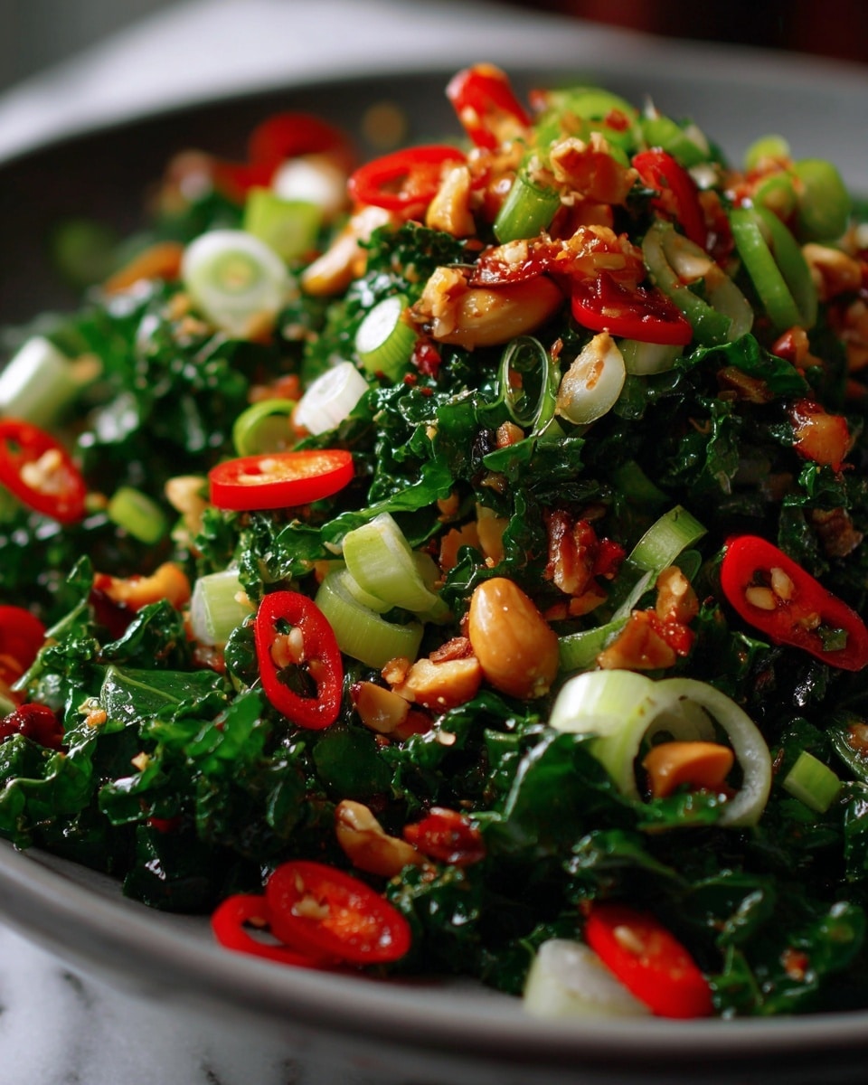This close-up image shows a colorful salad with many layers mixed together. The base layer is dark green leafy kale, chopped finely. On top of this are small pieces of light brown nuts, which look crunchy. Bright red slices of chili peppers are scattered evenly around the salad. There are also light green thin slices of scallions spread through the mix. The salad looks fresh with a light, shiny dressing coating the ingredients, giving a slightly wet texture. The photo has a white marbled background. photo taken with an iphone --ar 4:5 --v 7