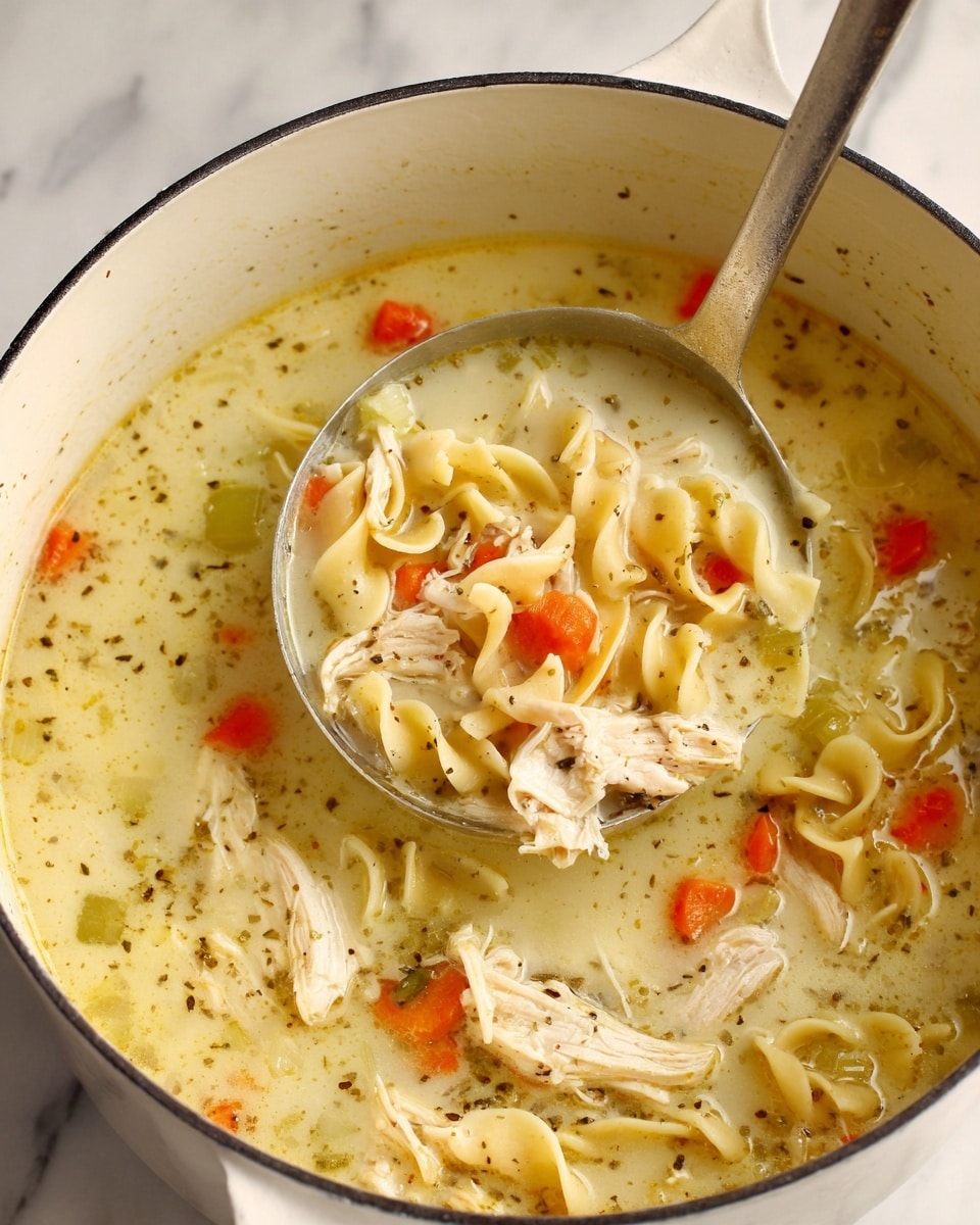 A thick soup with creamy beige broth filled with visible pieces of shredded light brown chicken, small orange carrot slices, pale yellow celery rings, and curly egg noodles in a large white pot with a metal ladle lifting a scoop of soup showing the mixed ingredients close up, the white marbled textured surface underneath visible around the pot, photo taken with an iphone --ar 4:5 --v 7
