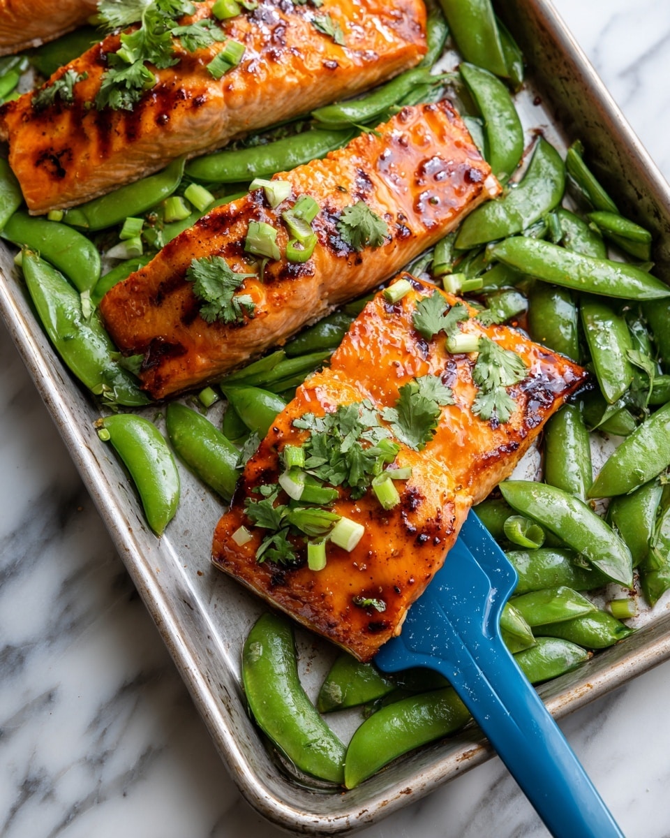 Three thick pieces of cooked salmon with a shiny, orange-brown glazed surface and small black grill marks sit on a metal baking sheet. Around the salmon, there are many bright green sugar snap peas scattered, some split open, with a few light green chopped scallion pieces and fresh cilantro leaves on top. One salmon piece is held by a dark blue spatula. The background is a white marbled texture. photo taken with an iphone --ar 4:5 --v 7