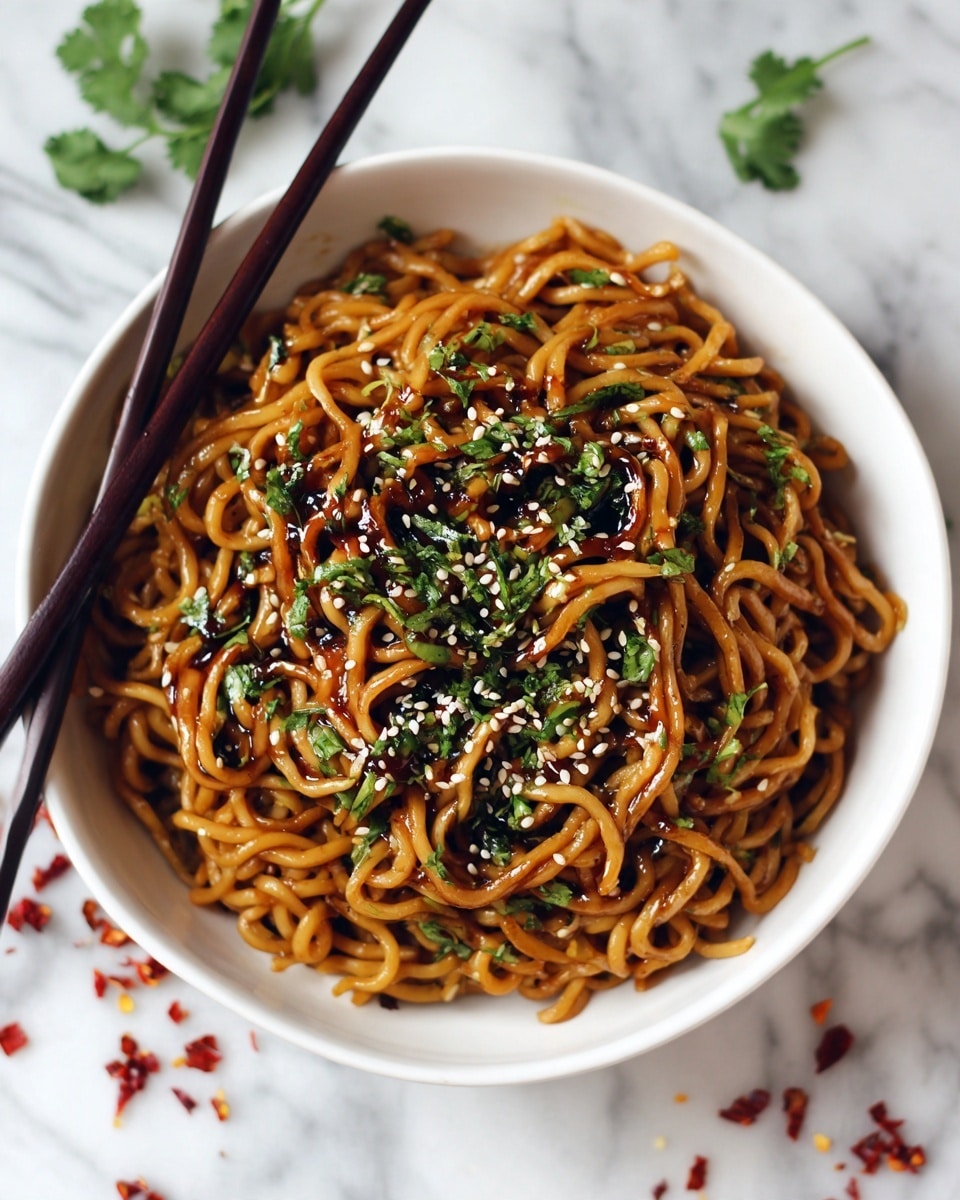 A white bowl is full of shiny cooked noodles coated in a rich brown sauce, mixed with small bits of green herbs and thin slices of green onion. The top layer has white sesame seeds sprinkled evenly and small red chili flakes scattered around. The bowl sits on a white marbled surface with small pieces of herbs and chili flakes spread casually nearby. A pair of black chopsticks rests on the left side of the bowl, leaning against the edge. photo taken with an iphone --ar 4:5 --v 7