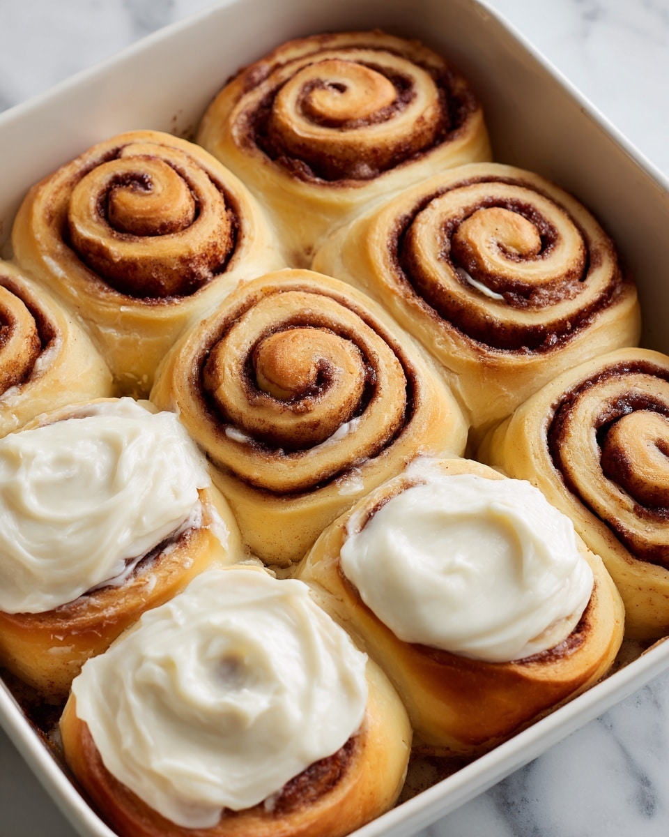 The image shows a close-up top view of nine cinnamon rolls arranged in a 3x3 grid on a white marbled surface. Each cinnamon roll has a golden-brown dough base with dark brown cinnamon spiral layers visible in the center. The top layer on most cinnamon rolls is thick, creamy white icing, spread unevenly with smooth and slightly swirled textures, while some rolls show the cinnamon layers more clearly where the icing is thinner or missing. The rolls appear soft and fluffy with a shiny glaze on the dough edges, and the spiral pattern is tight and distinct on each one. photo taken with an iphone --ar 4:5 --v 7