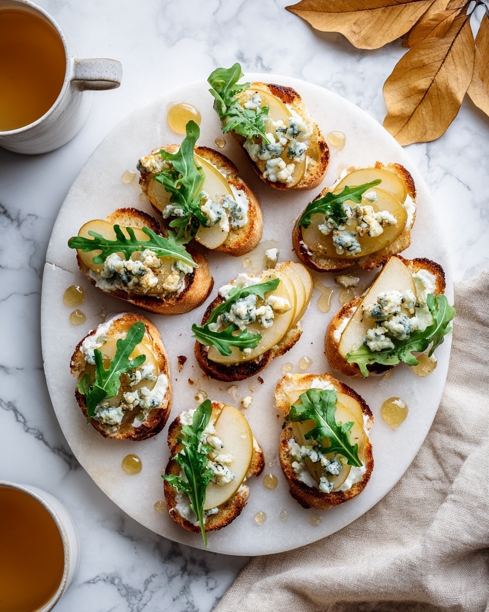 A round white plate with a white marbled texture holds ten small oval toasted bread slices arranged in a loose circular pattern. Each slice has a spread of soft white cheese, topped with a slice of light yellow pear, small crumbles of blue cheese, and a few fresh green arugula leaves. Golden honey is drizzled over the bread slices and the plate, adding shine and small drops scattered around. The background shows a white marbled surface with a couple of brown autumn leaves and a white cloth napkin. Two white bowls with light brown liquid sit near the plate. The overall look is fresh and colorful with white, green, yellow, blue, and brown tones. photo taken with an iphone --ar 4:5 --v 7