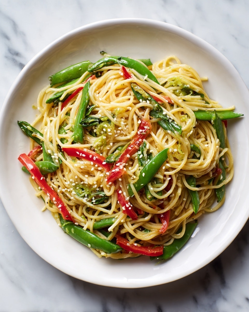 A white plate holds a close-up of a noodle dish with long, light yellow noodles spread evenly as the base layer. Bright red strips of bell pepper and fresh green snap peas and scallions are mixed throughout, adding pops of color. The dish is topped with small white sesame seeds scattered over everything. The background features a white marbled texture. photo taken with an iphone --ar 4:5 --v 7