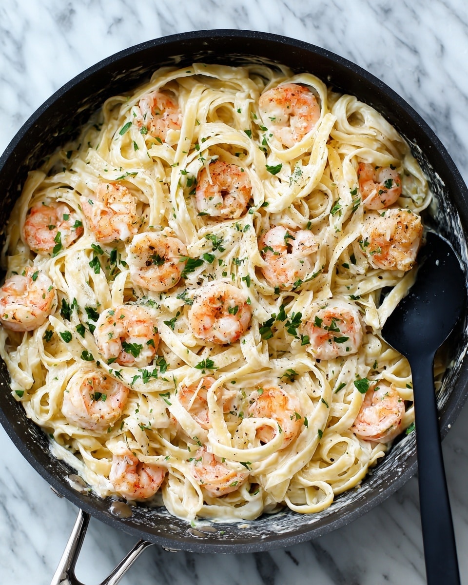 The image shows a pan filled with creamy white fettuccine pasta mixed with small pink shrimp scattered evenly throughout. The pasta strands are long and slightly curled, coated thoroughly in a thick white sauce. Small green parsley leaves are sprinkled on top, adding a touch of color. A black spoon is partially visible on the right side of the pan, resting on the pasta. The pan sits on a white marbled surface. Photo taken with an iphone --ar 4:5 --v 7