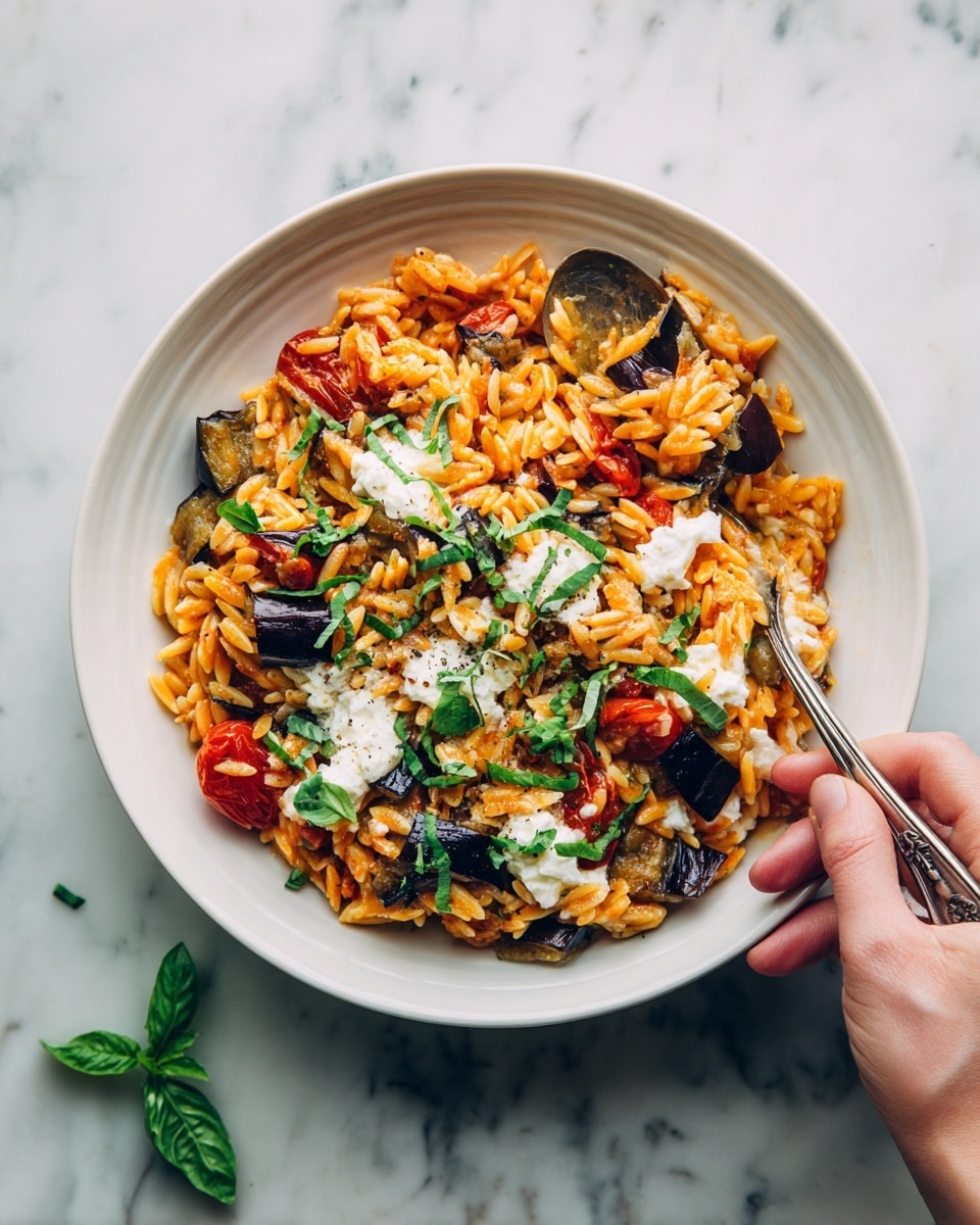 A bowl filled with three main layers: the base layer is orange-red orzo pasta mixed with tomato sauce, scattered with dark purple olives and pieces of roasted red peppers; the second layer is dollops of white creamy cheese spread unevenly on top, creating soft patches; the final layer is fresh green basil leaves placed on and around the pasta, adding a refreshing color contrast; the bowl is white and textured, and a silver spoon is partly submerged in the pasta, held by a pair of woman's hands, one holding the bowl and the other the spoon, all set on a white marbled surface; some extra basil leaves are casually placed near the bowl; photo taken with an iphone --ar 4:5 --v 7